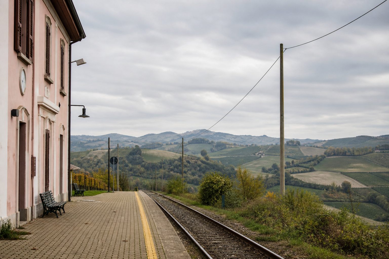 Banchina di una piccola stazione ferroviaria di campagna con binario unico e colline sullo sfondo