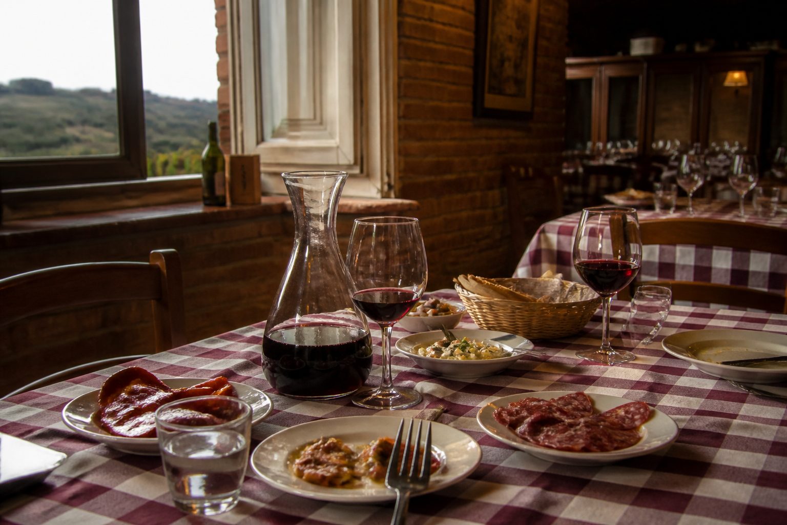 Tavola apparecchiata in una trattoria rustica con più piattini di antipasto, caraffa di vino rosso e tovaglia a quadri