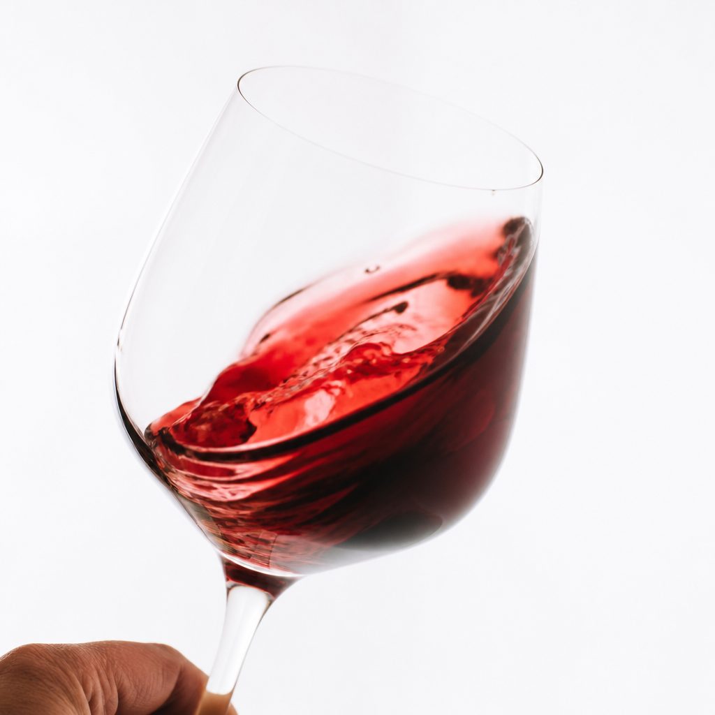 Vino fatto roteare nel calice davanti a uno sfondo bianco, con gli archetti visibili sulla parete interna