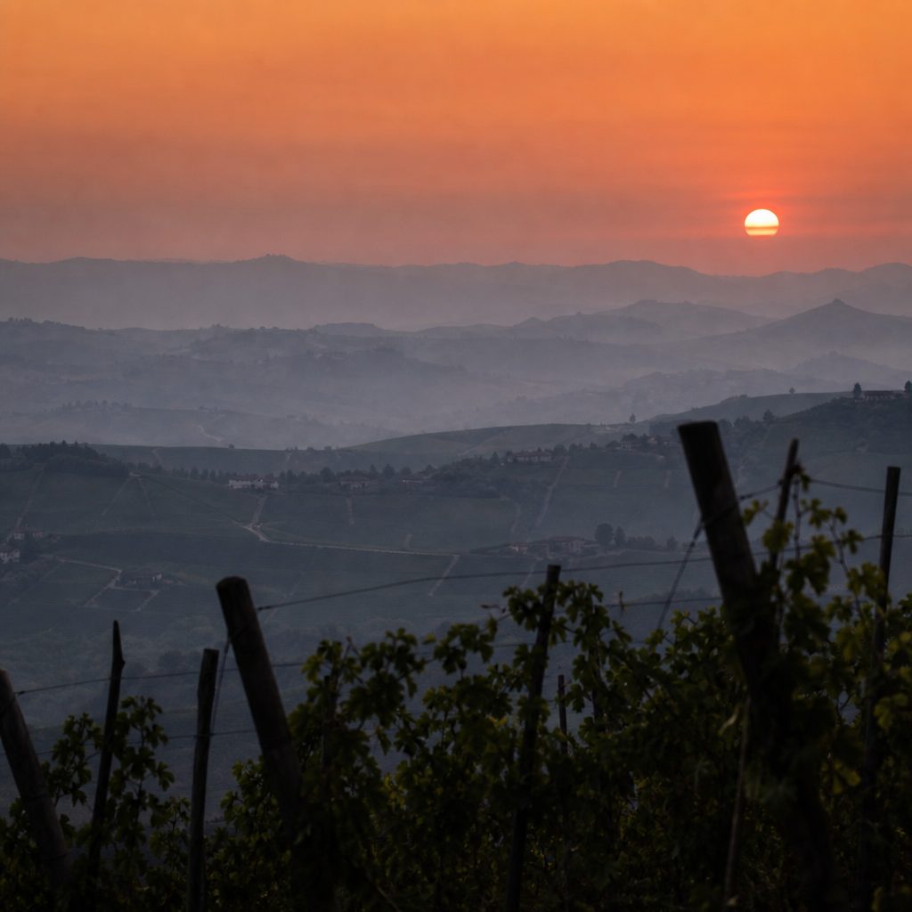 Tramonto da una collina sopra crinali sovrapposti, con il sole schiacciato dalla foschia