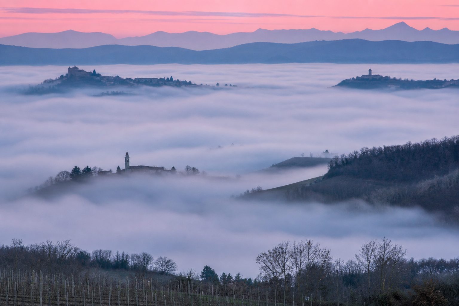 Mare di nebbia che riempie le vallate all'alba, con solo le cime delle colline e i campanili emergenti