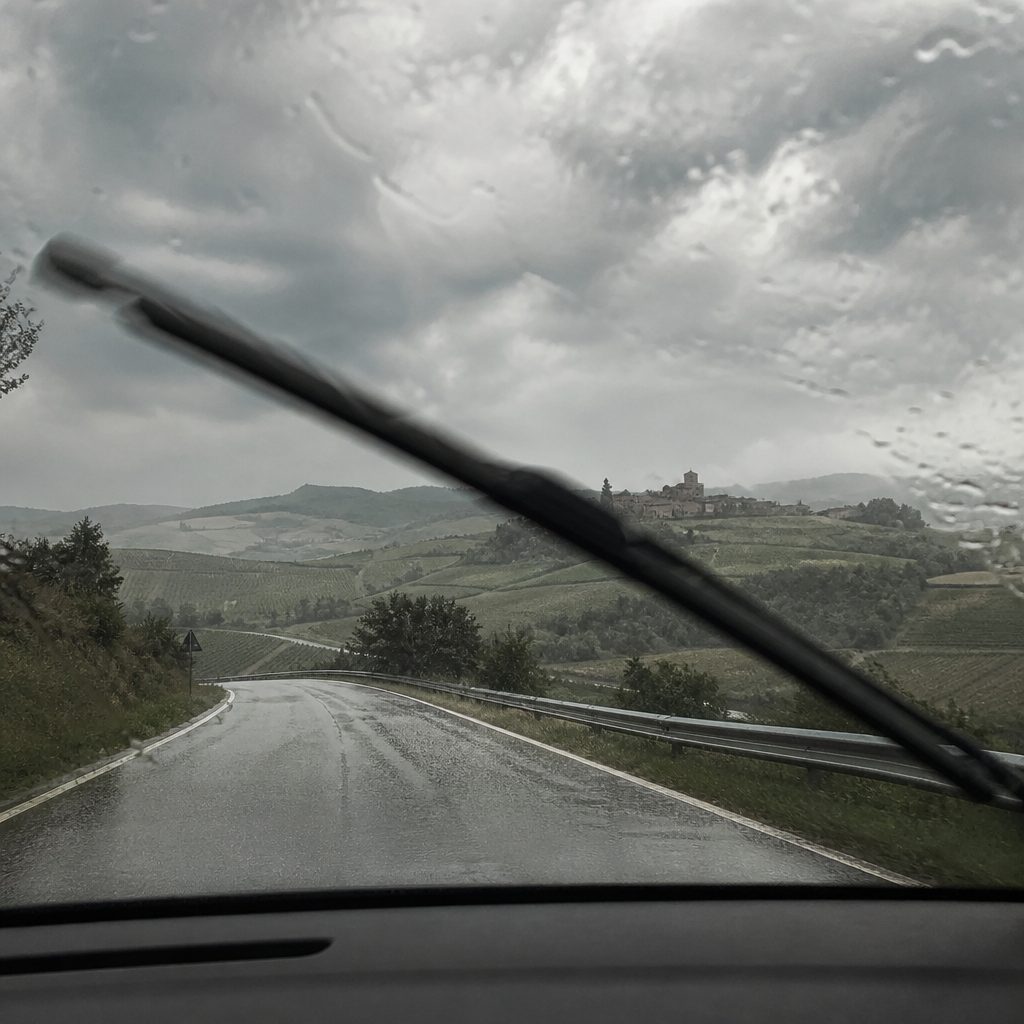 Pioggia battente su una strada di campagna vista dal parabrezza di un'auto, tergicristalli in movimento