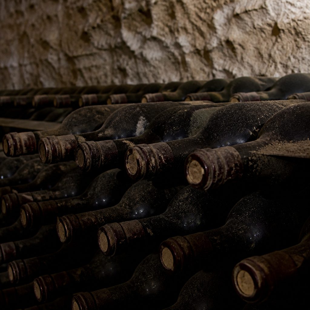 Bottiglie impolverate coricate in una rastrelliera di cantina, senza etichette leggibili